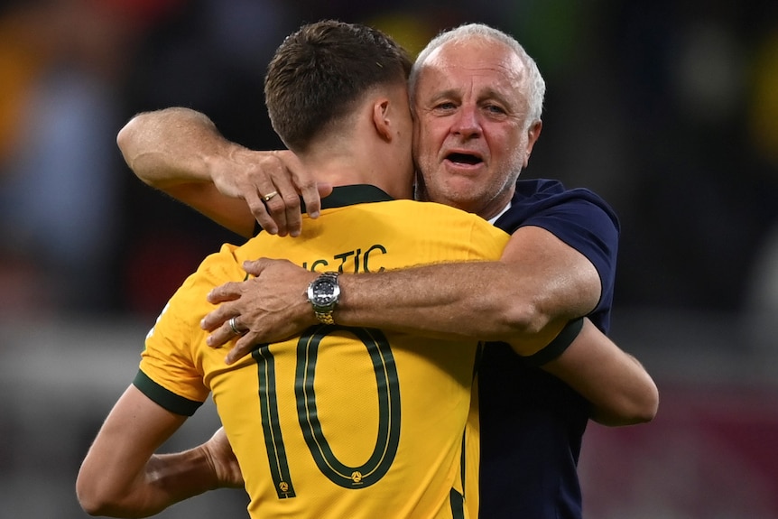 Two men, one wearing a yellow and green shirt, hug