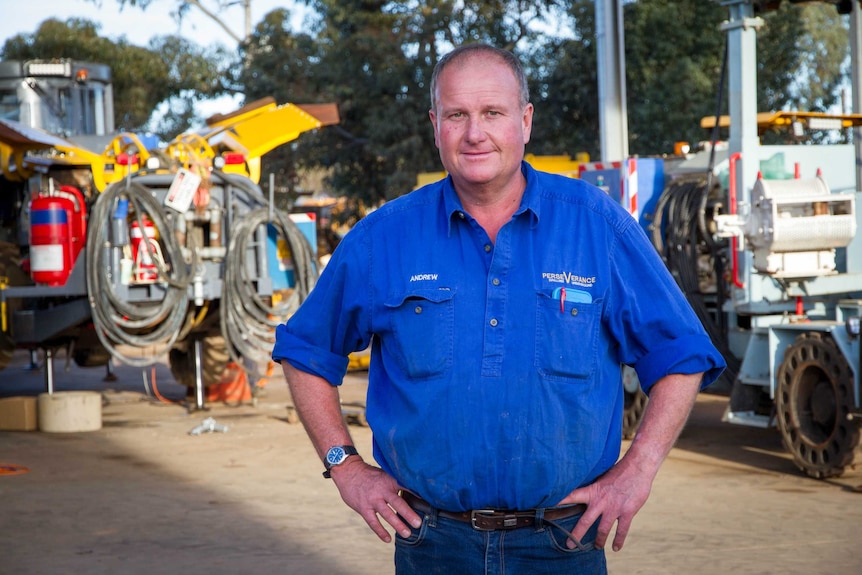 A mid-shot of Perseverance Drilling managing director Andrew Smith posing for a photo in front of drilling equipment.