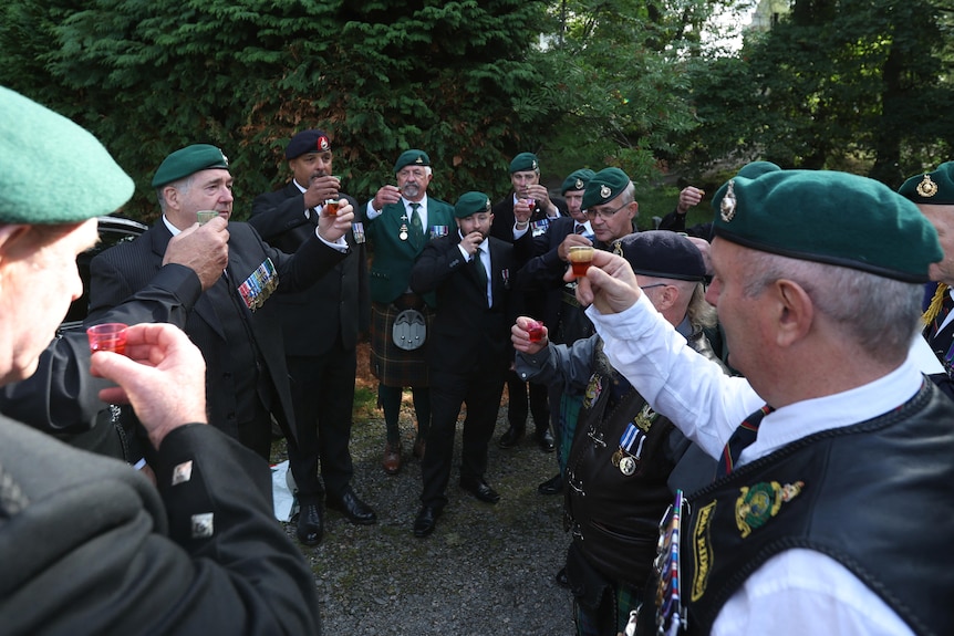 People in military uniforms raise a toast on a country road 