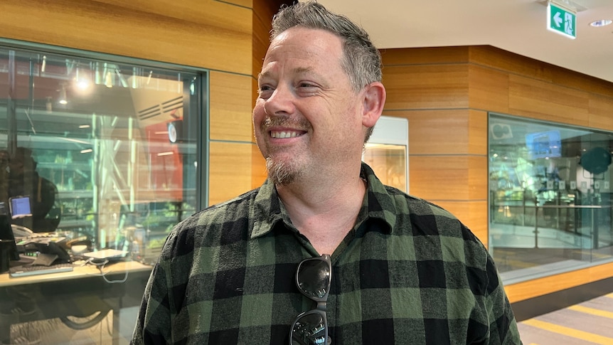 A man in a green shirt smiles in front of a wall of glass