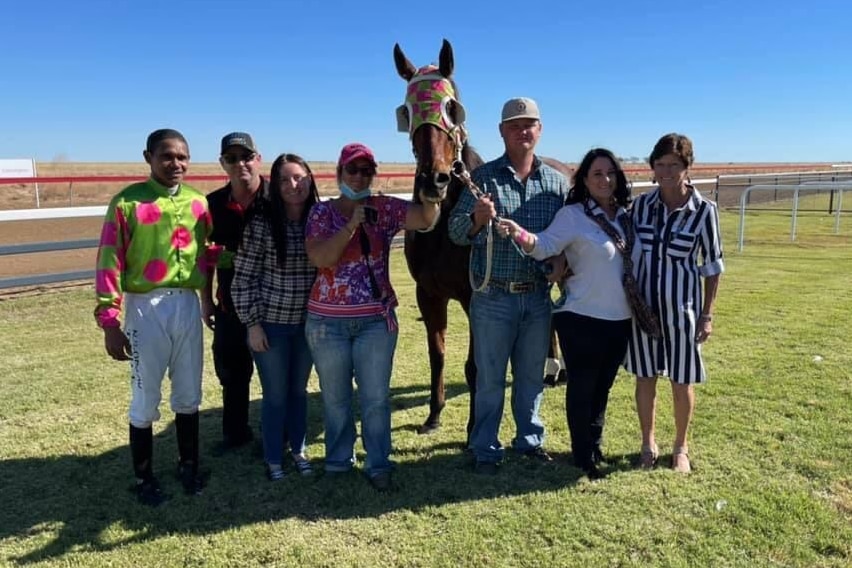 Group of people stand together with a racehorse at a racetrack in Julia Creek