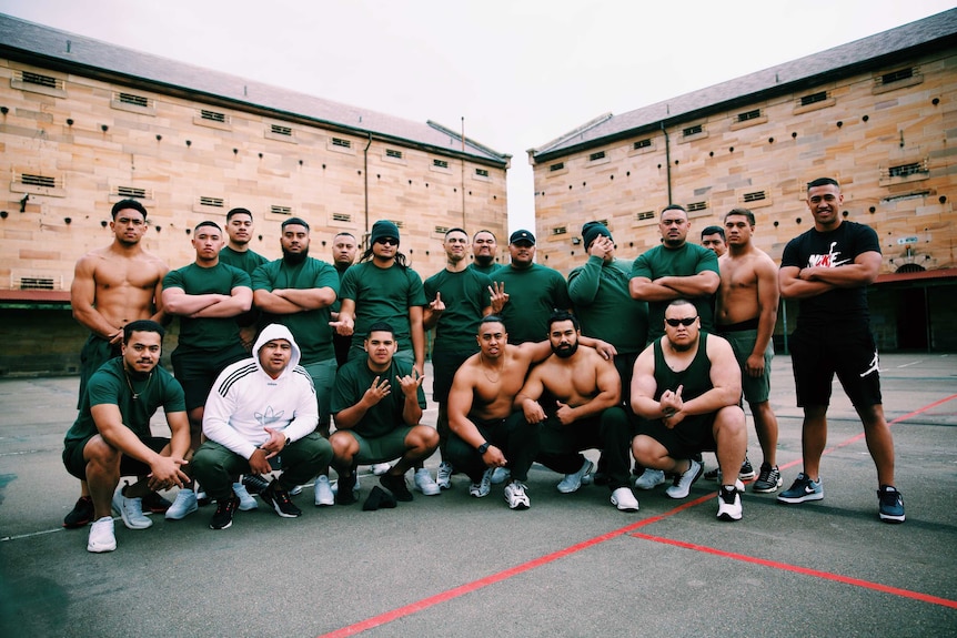 A group of young men pose in prison green-style costumes, including members of OneFour.