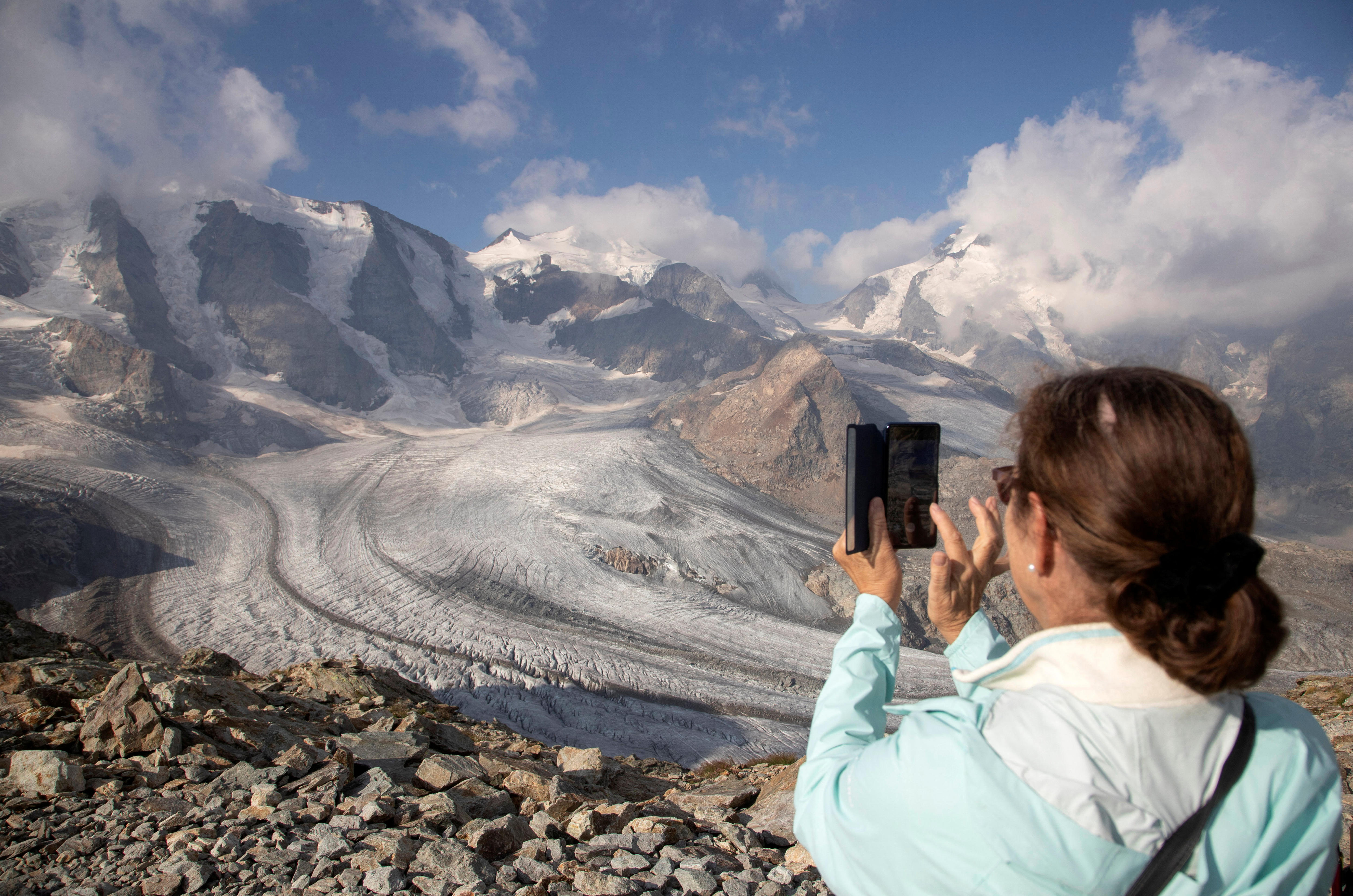 A woman in a blue jacket takes a photo of the Swiss alps with her mobile phone. 