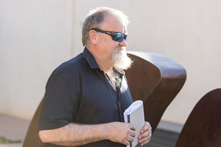 A man wearing sunglasses with a goatee beard leaves a courthouse.  