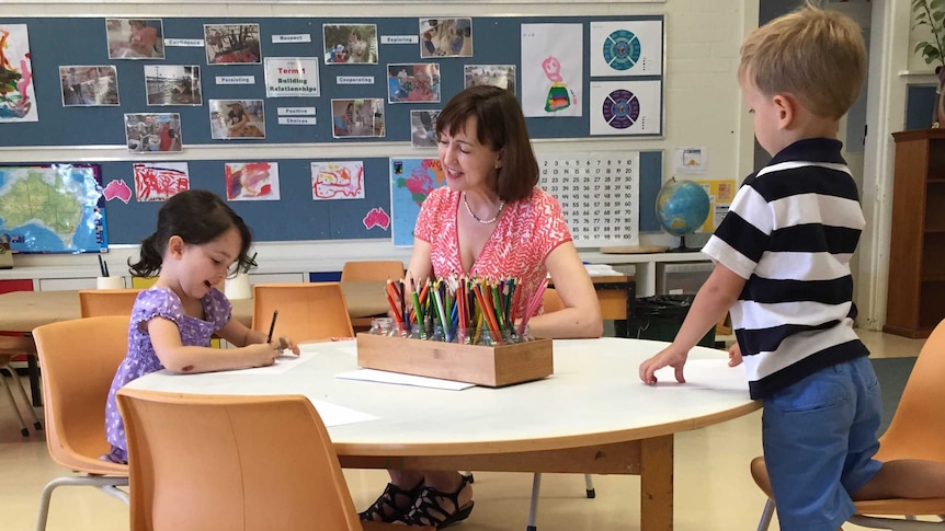 Education Minister Susan Close sits with kinder pupils at a little table and chairs.