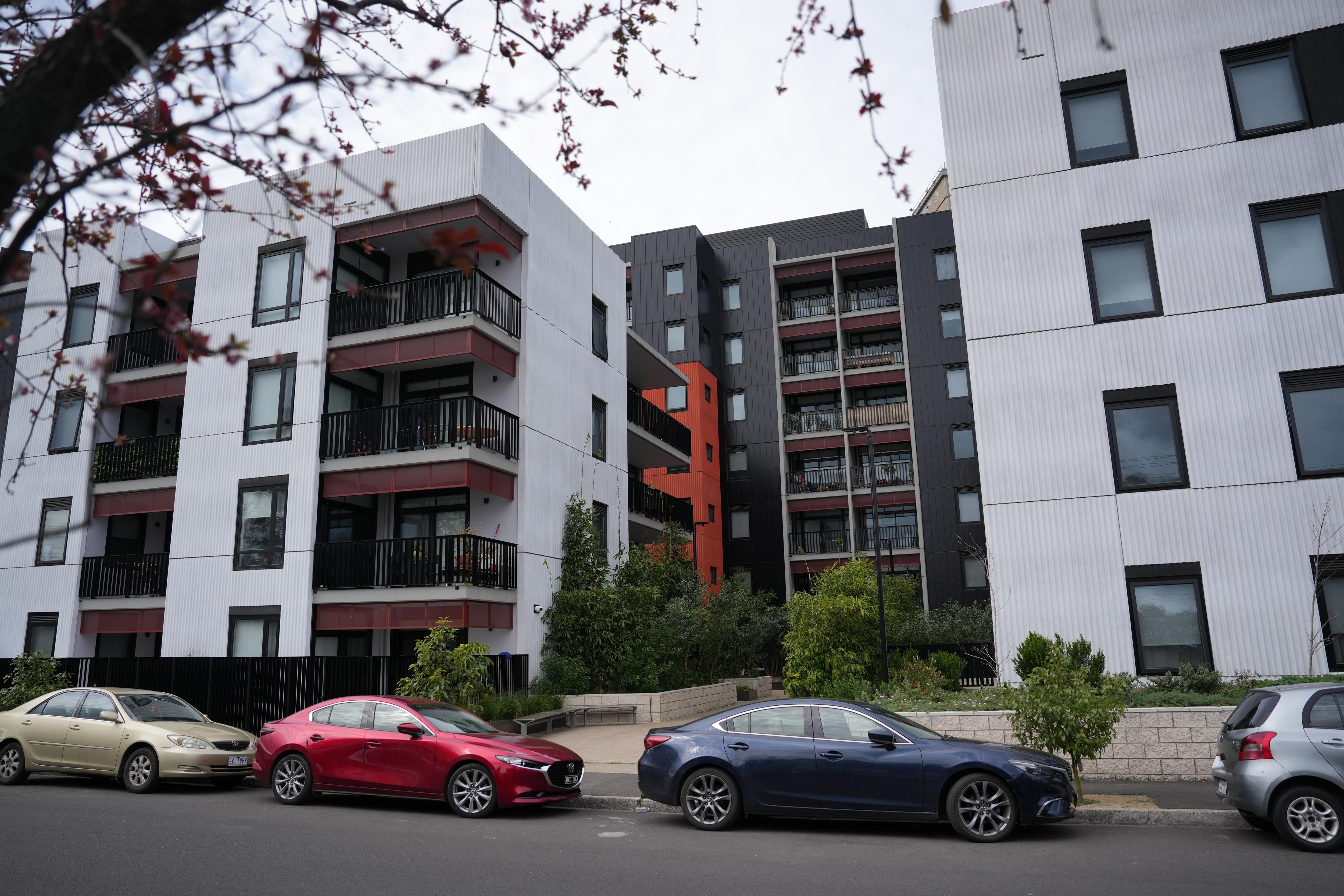 A modern four-storey housing development with cars parked on the street in front.