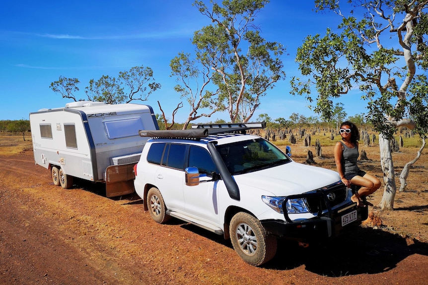 Julie Thalmann sits on the bonnet of her car, caravan in tow.