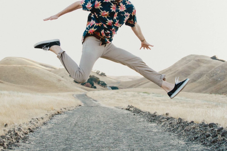 A man wearing khaki chinos jumps in the air, an example of a classic casual men's weekend outfit.