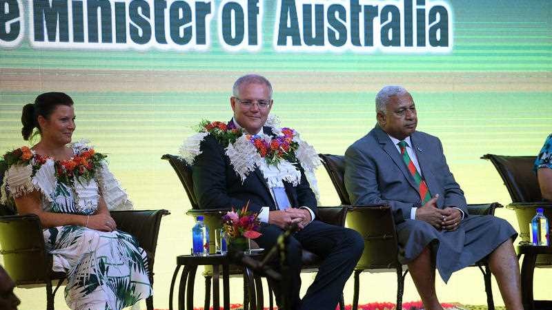 Scott Morrison sits on a stage with his wife Jenny and Fiji Prime Minister Frank Bainimarama