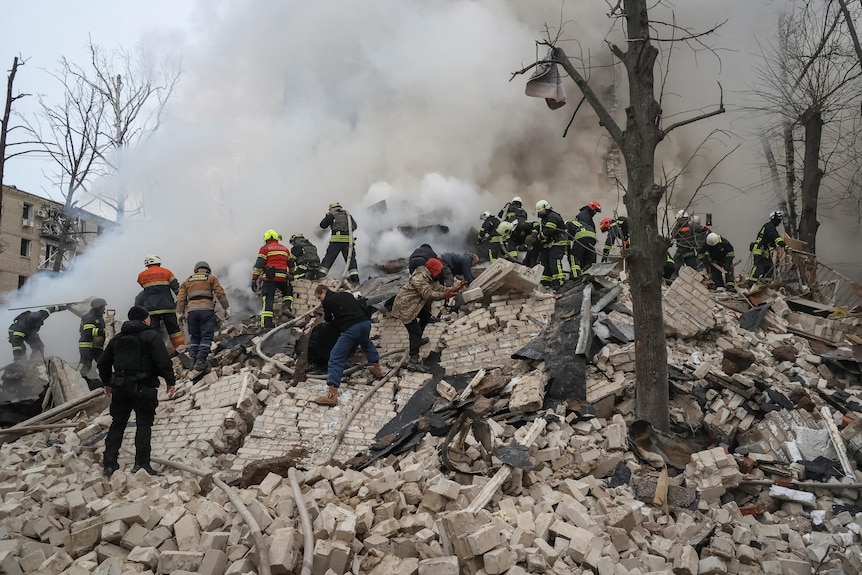 Emergency service personnel stand atop rubble.