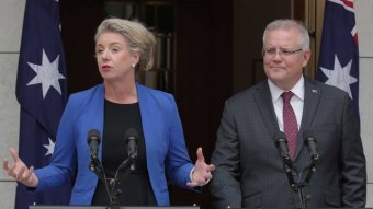 Bridget McKenzie and Scott Morrison stand at lecterns in a courtyard with Australian flags behind them.
