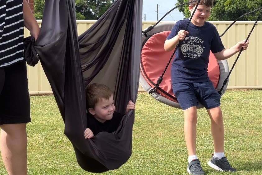 Two boys on swings with grass behind them