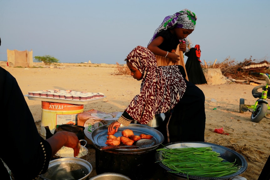 A girl picks food prepared by her mother at a camp