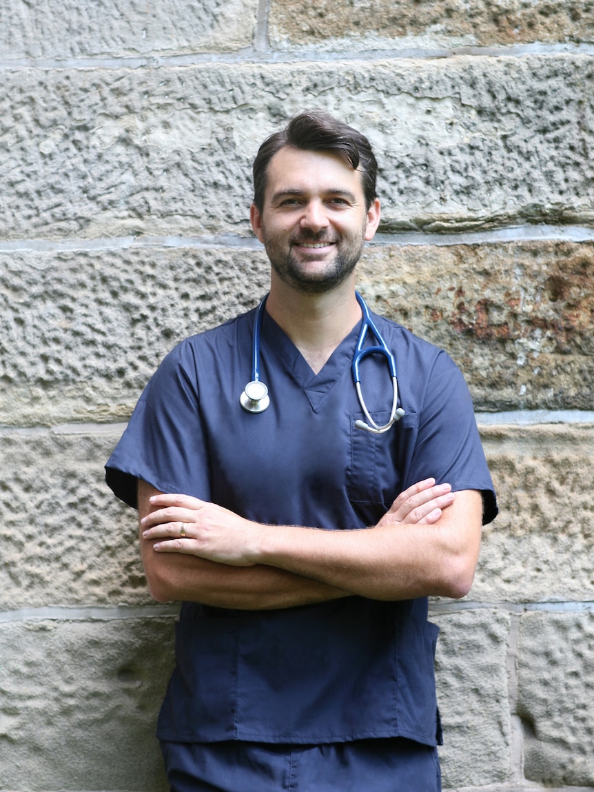 Dr Ben Bravery stands posing for photo in medical scrubs