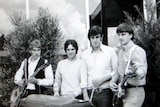 black and white photo of four men standing side by side holding instruments