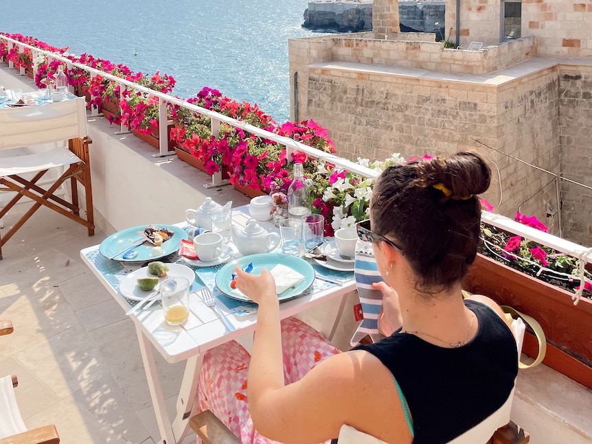 A woman sitting on a balcony overlooking the ocean