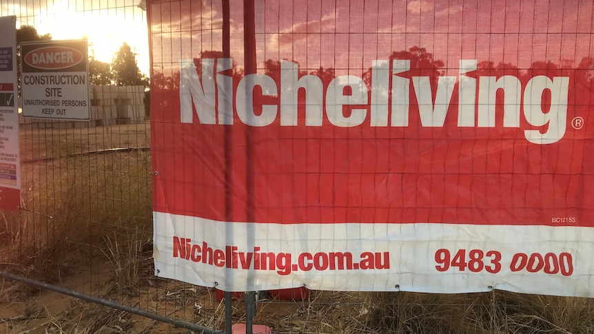 Large NicheLiving sign hanging from fence sunset in background