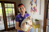 A woman holding a white and ginger cat in her arms smiles at the camera. 
