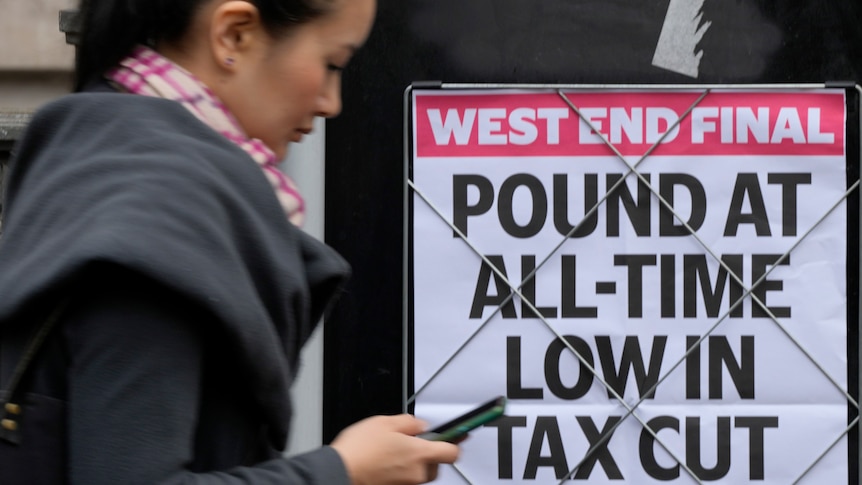 Woman with phone in hand walks by UK news headline about pound being at all time low.