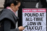Woman with phone in hand walks by UK news headline about pound being at all time low.