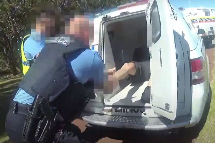 A police officer grabs onto the legs of a man in the back of a police van