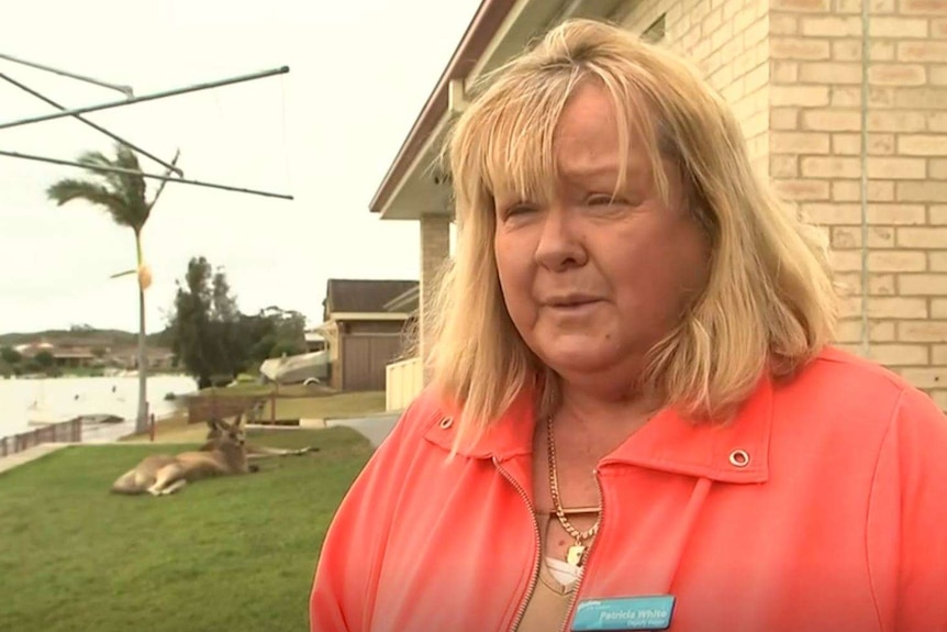 Shoalhaven Deputy Mayor, Patricia White standing outside her home, with a flooded river in the background and a kangaroo.