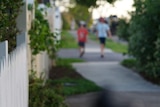 Two anonymous primary school-aged boys walk in distance along a suburban street with houses in Australia.