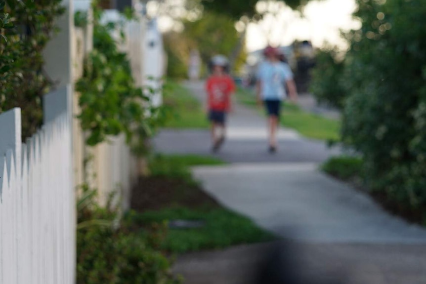 Two anonymous primary school-aged boys walk in distance along a suburban street with houses in Australia.