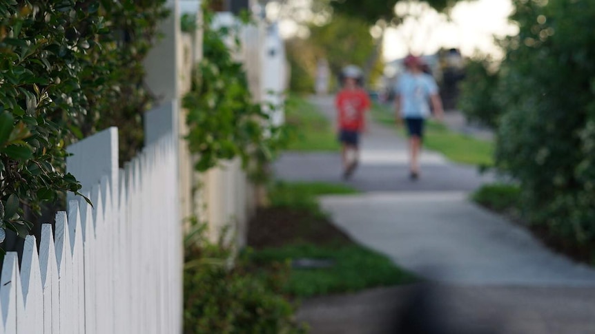 Two anonymous primary school-aged boys walk in distance along a suburban street with houses in Australia.
