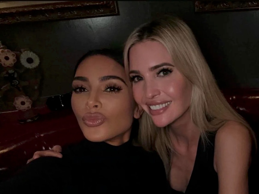 Kim Kardashian makes a duck face while Ivanka Trump places her hands on Kim's shoulders and smiles.