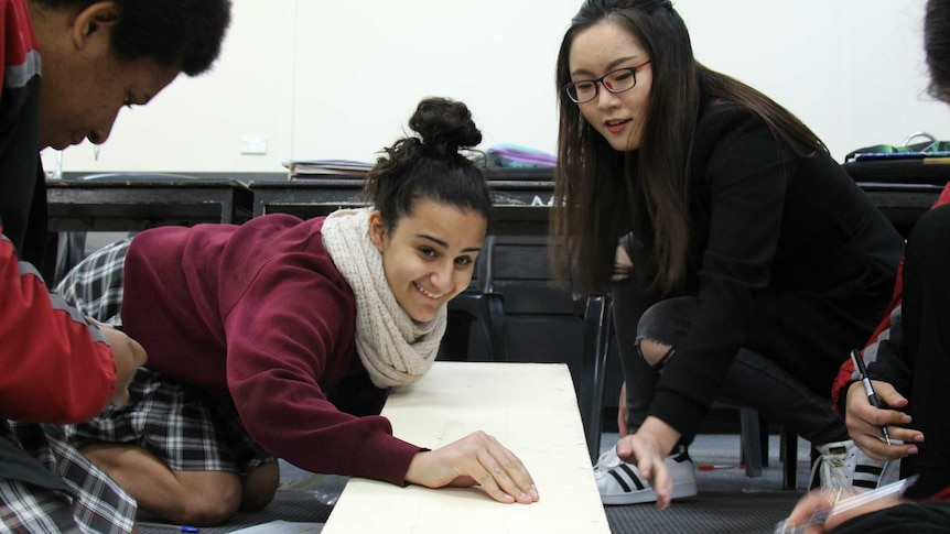 A Year 9 student (left) holds a marble at the top of a ramp. Lori Lu (right) looks on.