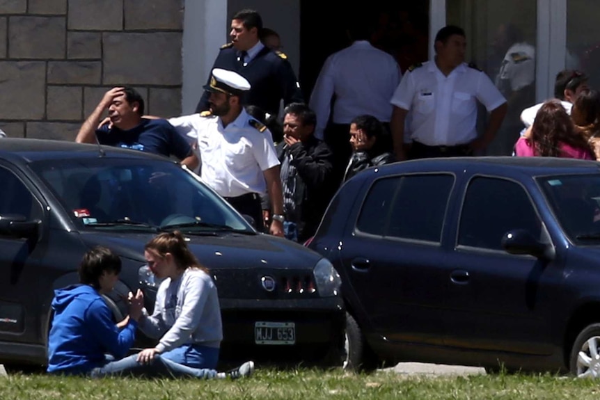 Civilians and navy officers gather, crying outside a naval base.