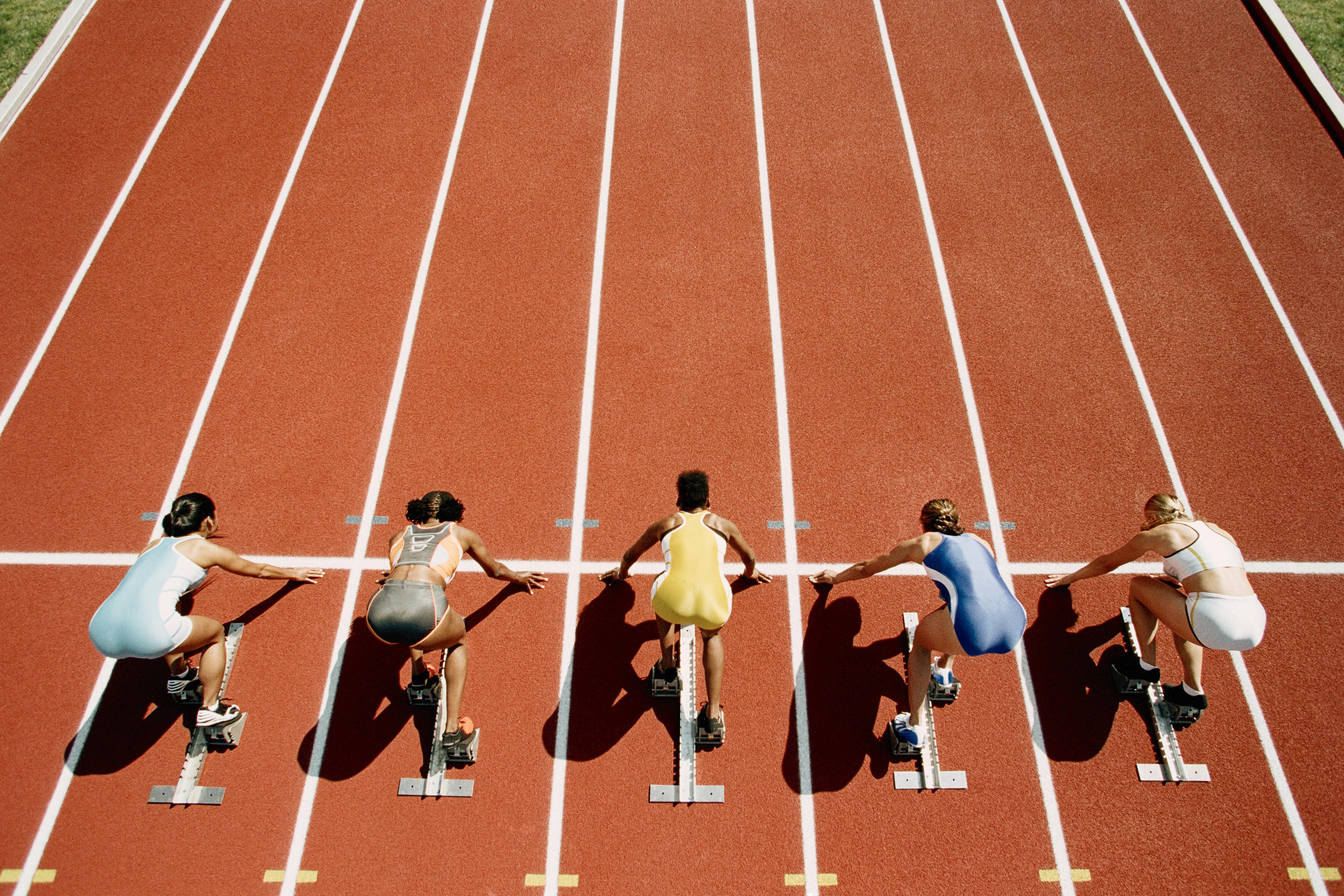 5 runners crouching at the start of a running track. They're positioned ready to take off. 