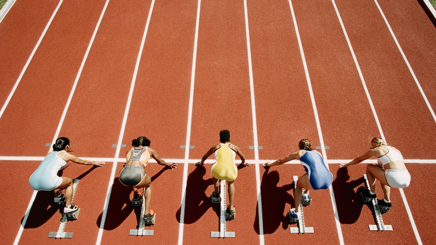 5 runners crouching at the start of a running track. They're positioned ready to take off. 