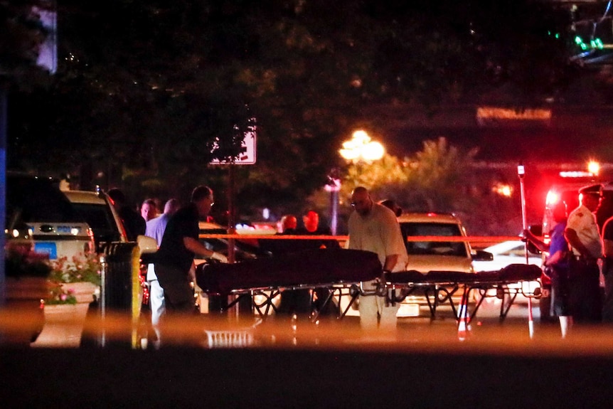 Officials are seen wheeling people out in body bags with flashing lights in the backdrop.