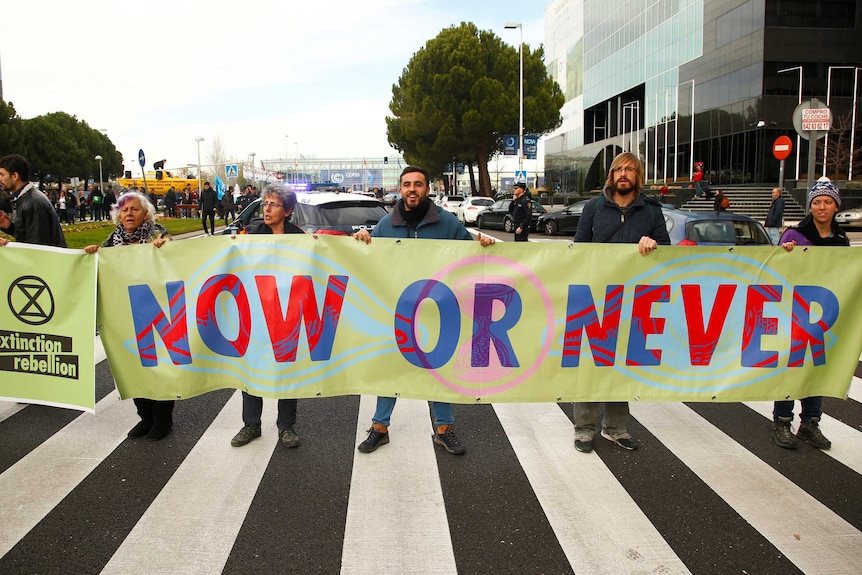 People hold a sign in the street that reads 'Now or Never'.