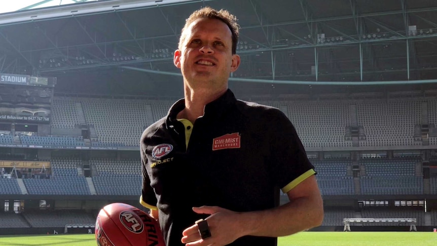 An umpire, wearing an AFL shirt and holding a football.