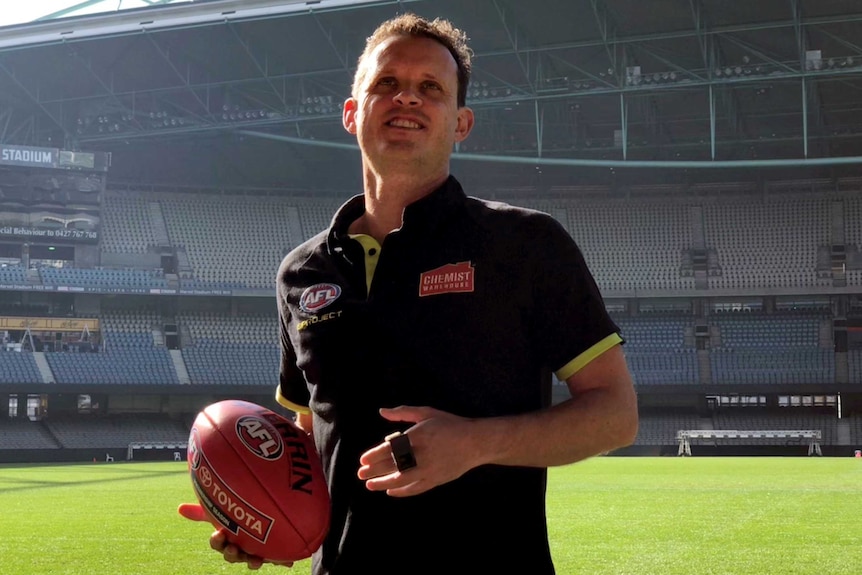 An umpire, wearing an AFL shirt and holding a football.