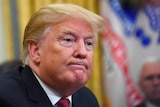 Donald Trump stares out of the frame with a mild grimace. Mike Pence can be seen in the blurred background.