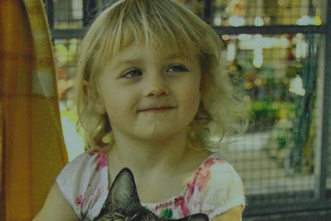 Four year old girl with blue eyes and wavy blonde hair nursing a tortoise shell cat.