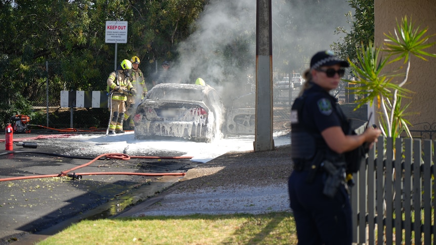 Firefighters using foam to put out a car fire on a dead end street as a police office looks on