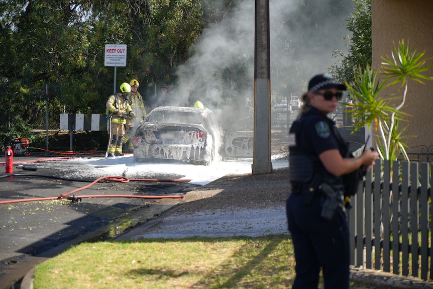 Firefighters using foam to put out a car fire on a dead end street as a police office looks on