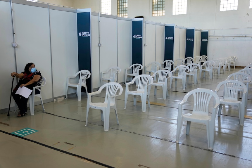 A woman sits in the nearly empty waiting room of a vaccination centre 