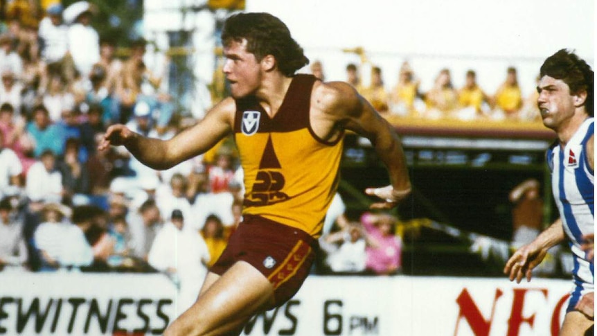 AFL player in Brisbane Bears uniform kicking on field in front of an audience.