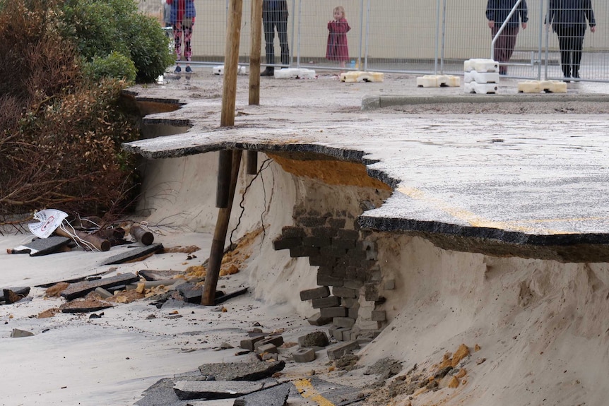 A badly eroded car park overhanging a beach that has had lots of sand washed away underneath it.