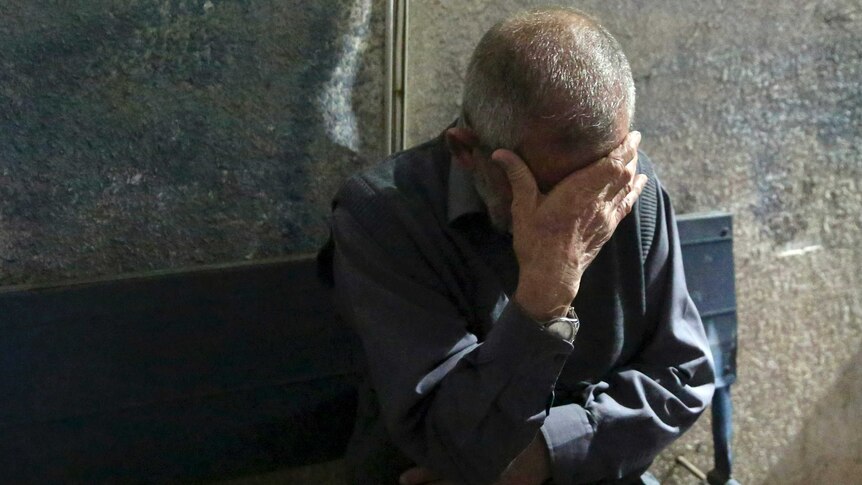 A man with short, grey hair covers his eyes with one hand in grief.