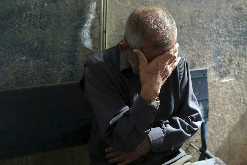 A man with short, grey hair covers his eyes with one hand in grief.