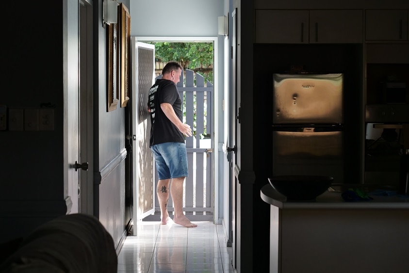 Silhouette image of middle aged man opening front door to his house from inside a hallway.