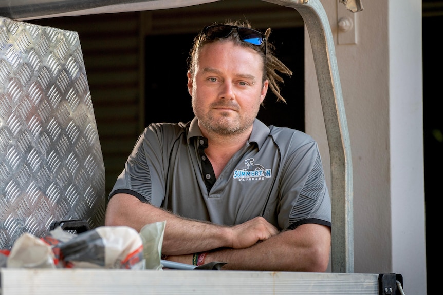 A man leans on the tray of a ute and looks at camera with arms crossed
