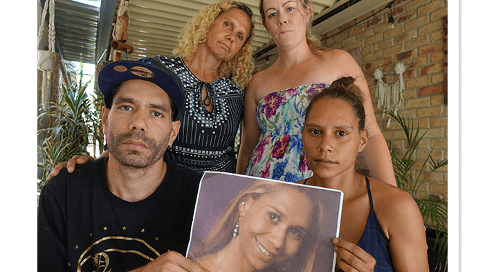 Two women standing, one man and woman sitting holding photograph of you missing indiegnous woman.